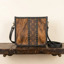 Load image into Gallery viewer, A crossbody bag with a brown Dark Brindle Cowhide panels, a central brown monogram canvas stripe, and Dark brown leather trim. Cowhide is unique and may vary slightly per order.